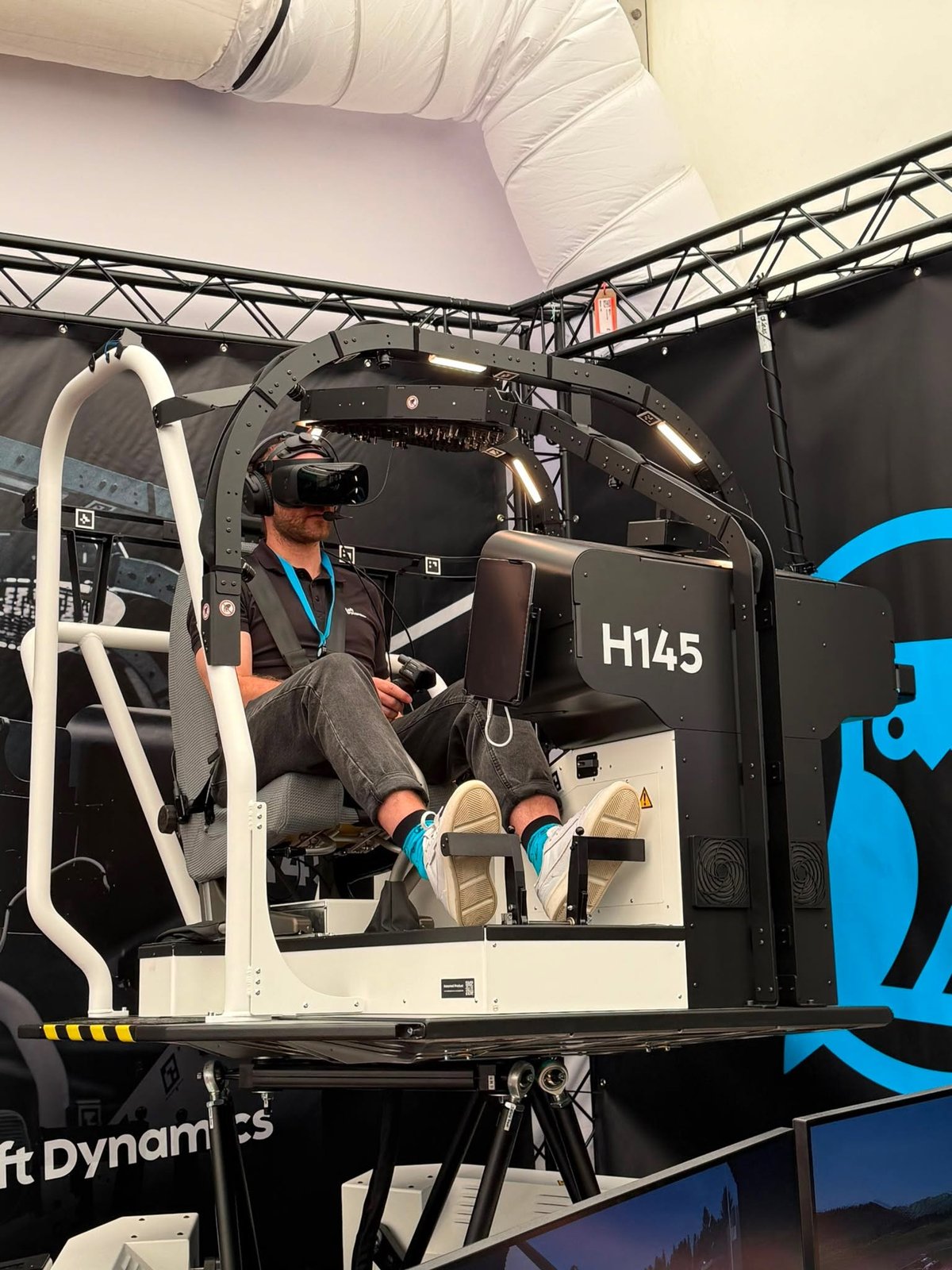 A team member in the outfit flying the H145 simulator at the booth, with the dark backdrop and the owl logo
