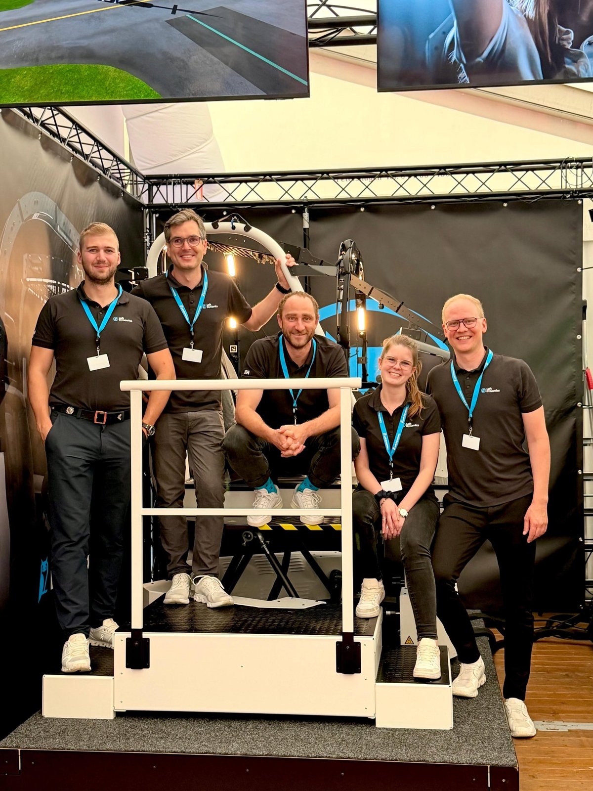The Loft Dynamics team in the new trade-show outfit at the booth, in front of a simulator
